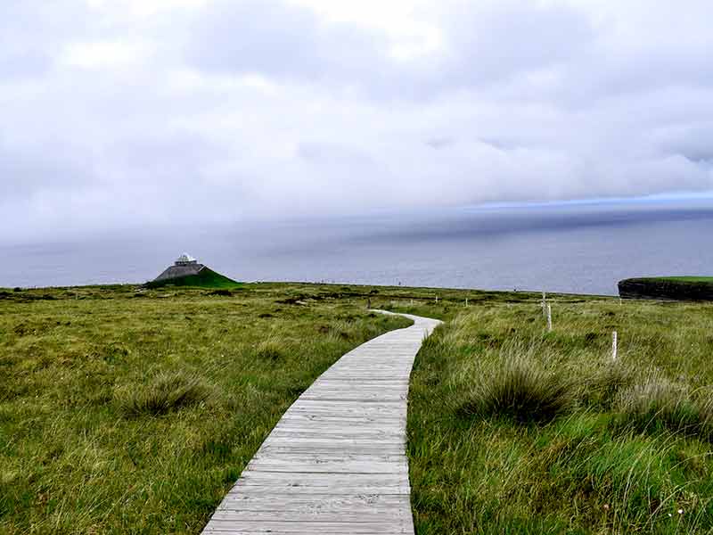 A boardwalk over a grassy bog leading to a triangular shaped visitor centre
