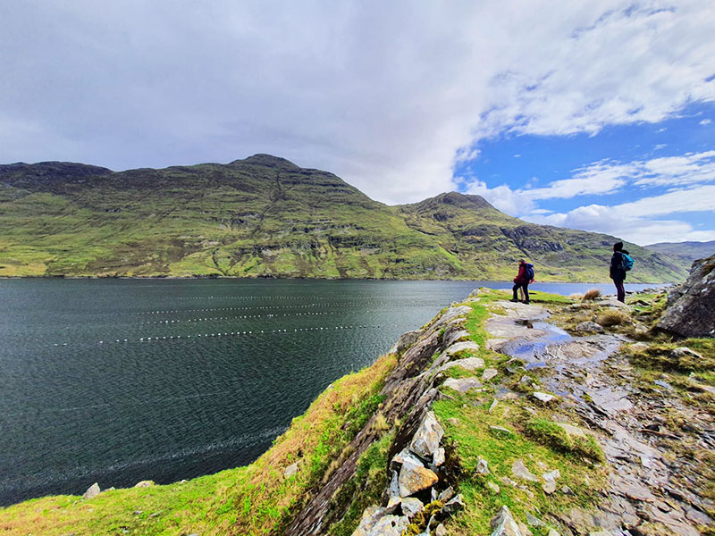 Two hikers on the shores of Killary fjord with dramatic mountains